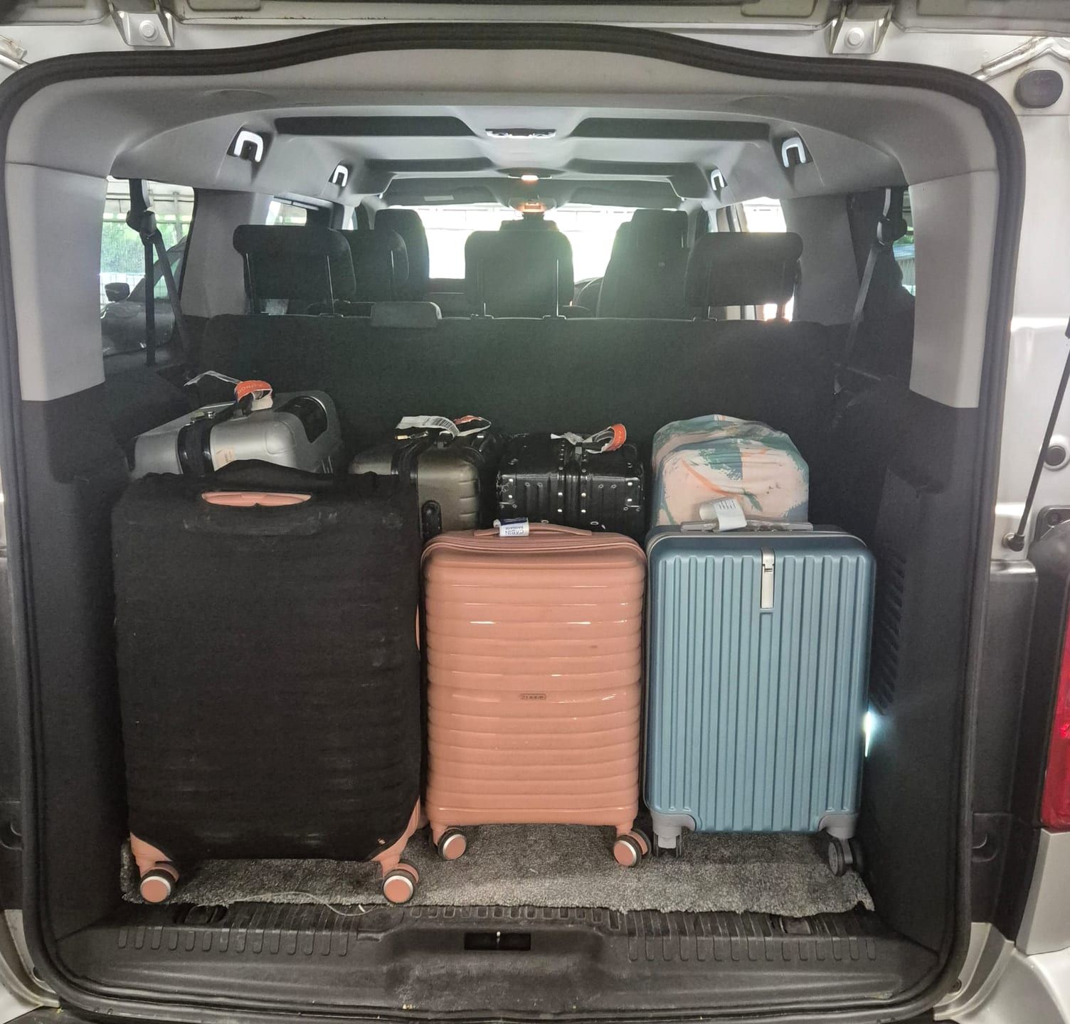 Suitcases loaded in the open boot of a minibus.